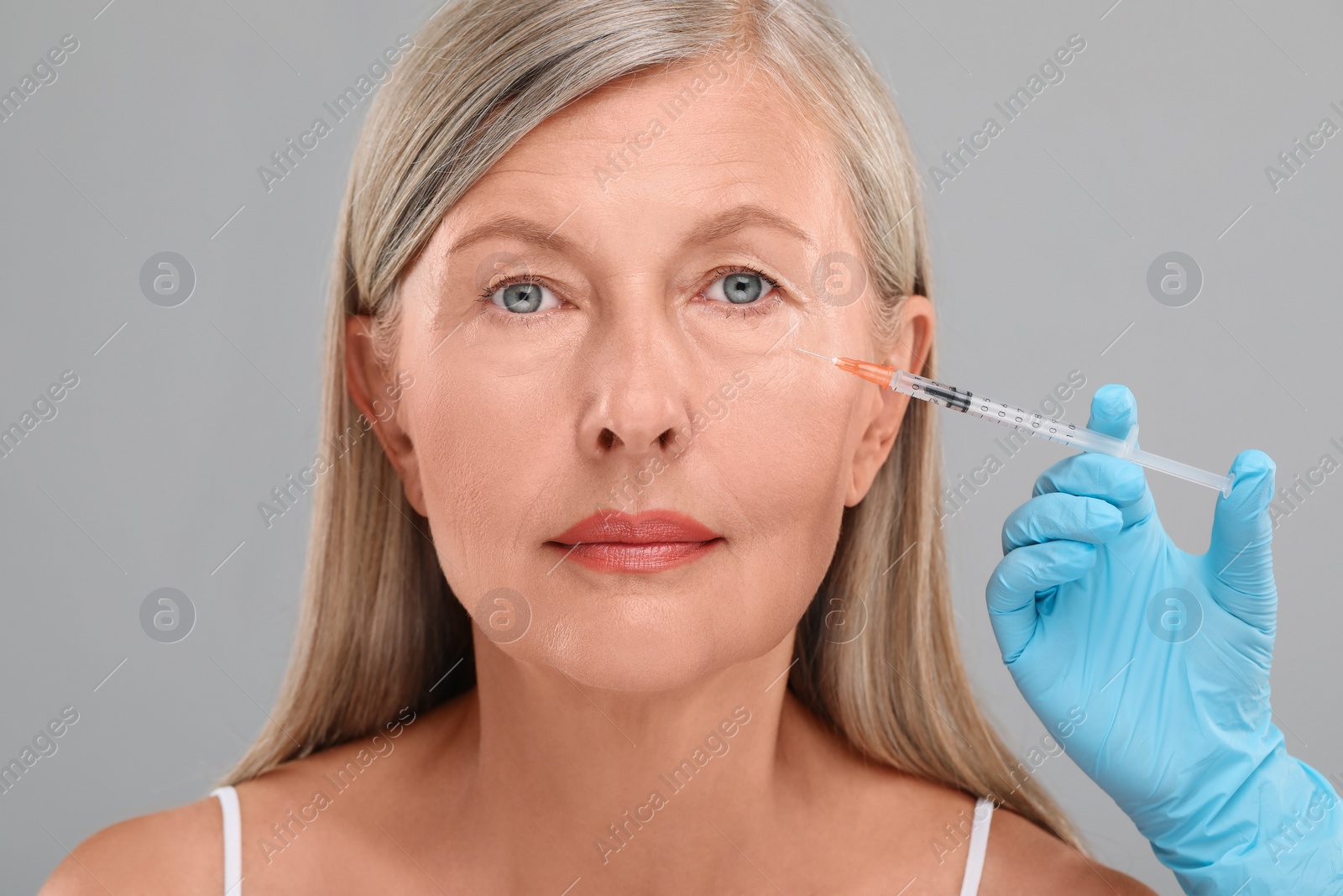 Photo of Doctor giving facial injection to senior woman on light grey background, closeup. Cosmetic surgery