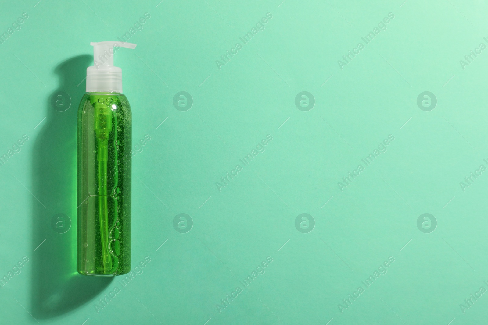 Photo of Bottle of green cosmetic gel on turquoise background, top view. Space for text