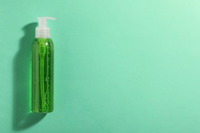 Bottle of green cosmetic gel on turquoise background, top view. Space for text