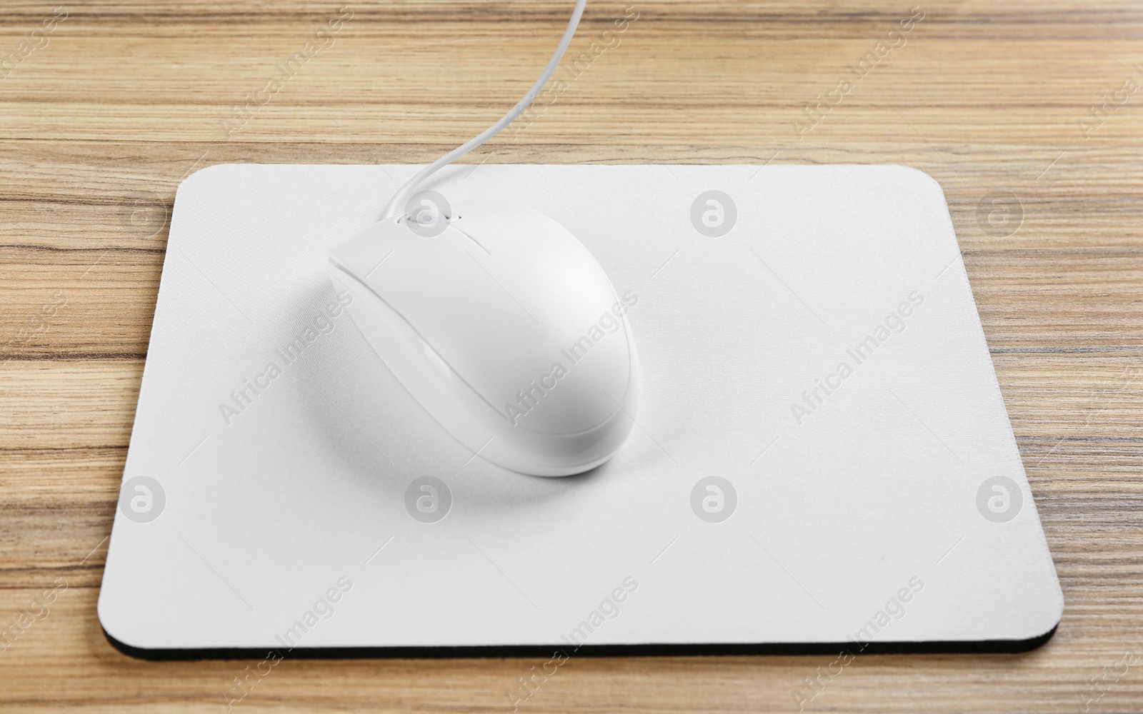 Photo of Modern wired optical mouse and pad on wooden table