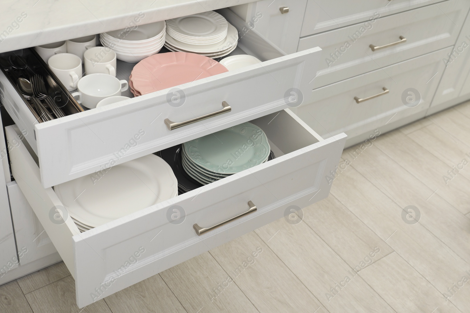 Photo of Clean plates, bowls, cutlery and cups in drawers indoors