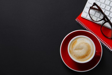 Cup with aromatic cappuccino, notepad, keyboard and glasses on black background, flat lay. Space for text