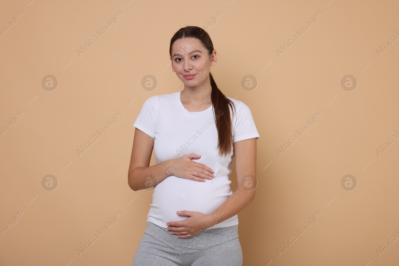 Photo of Beautiful pregnant woman in white T-shirt on beige background
