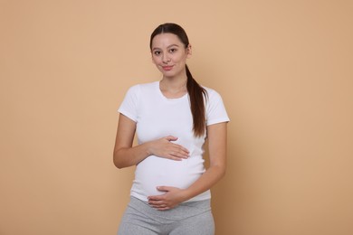 Beautiful pregnant woman in white T-shirt on beige background