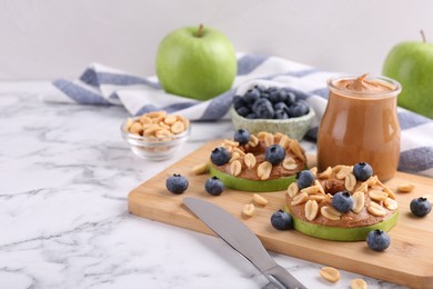 Fresh green apples with peanut butter, blueberries and nuts on white marble table, space for text