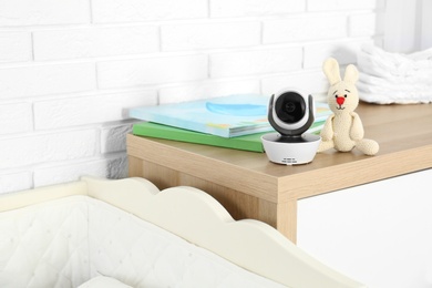 Photo of Baby camera with books and toy on chest of drawers near crib in room, space for text. Video nanny