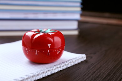 Kitchen timer in shape of tomato and notebook on wooden table, closeup. Space for text