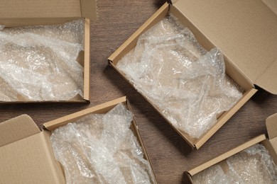 Photo of Many open cardboard boxes with bubble wrap on wooden table, flat lay