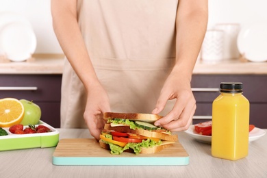 Photo of Woman preparing food for her child at table in kitchen, closeup. Healthy school lunch