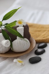 Spa stones, flowers and herbal bags on towel indoors, closeup