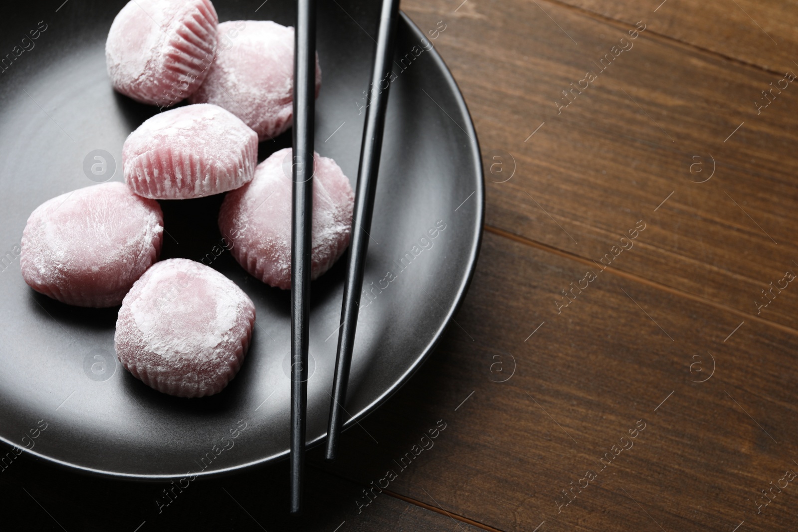 Photo of Black plate with delicious mochi and chopsticks on wooden table, space for text. Traditional Japanese dessert