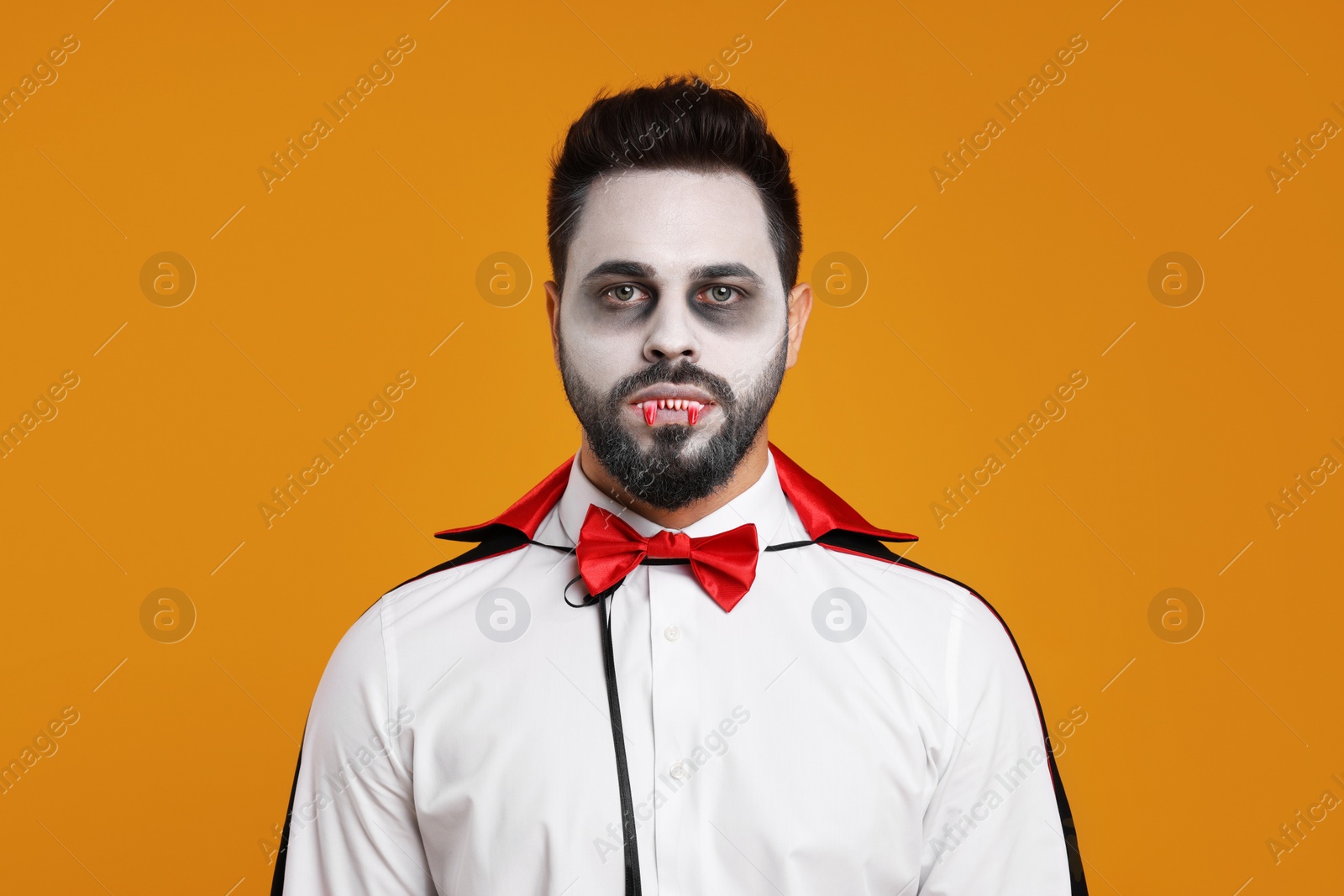 Photo of Man in scary vampire costume with fangs on orange background. Halloween celebration