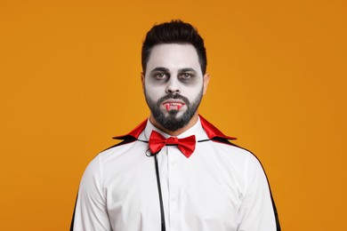 Photo of Man in scary vampire costume with fangs on orange background. Halloween celebration
