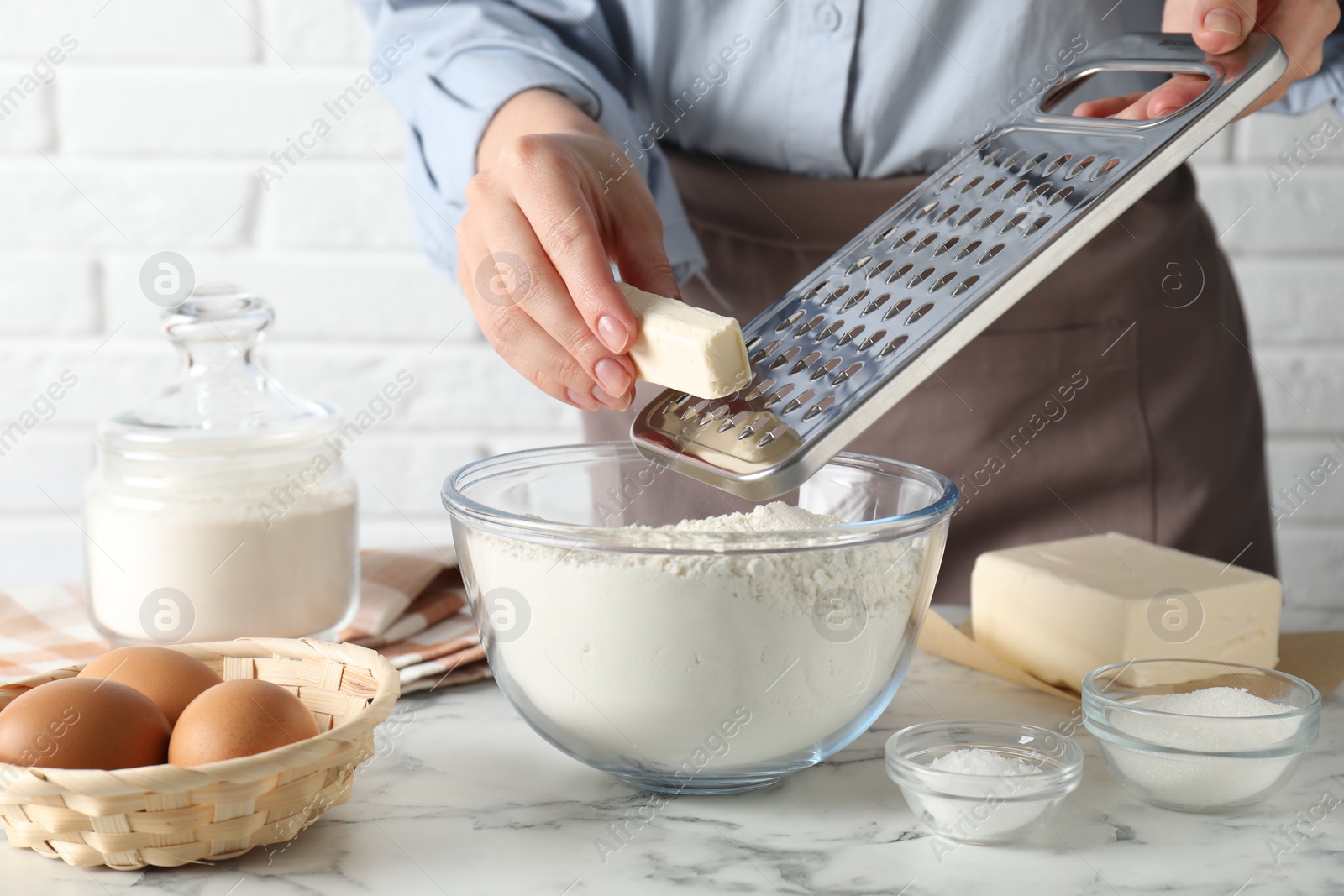 Photo of Woman grating butter into bowl with flour at white marble table, closeup