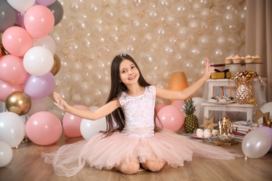 Photo of Happy little girl sitting on floor in beautifully decorated room at home. Birthday celebration