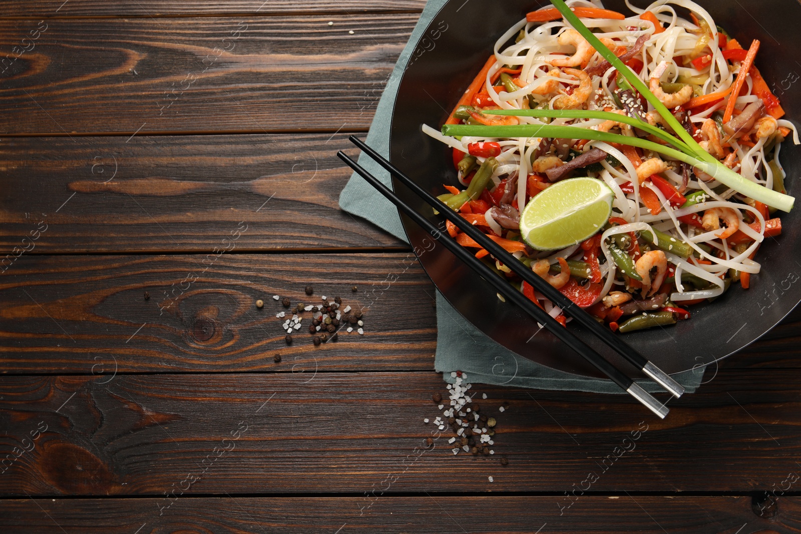 Photo of Shrimp stir fry with noodles and vegetables in wok on wooden table, top view. Space for text