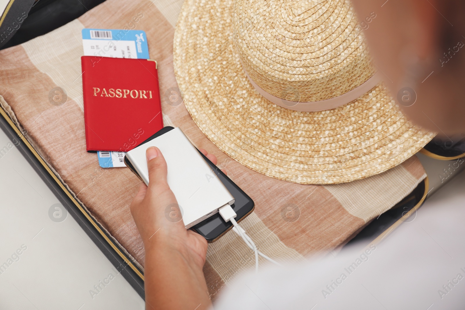 Photo of Woman charging smartphone with power bank near packed suitcase indoors, closeup