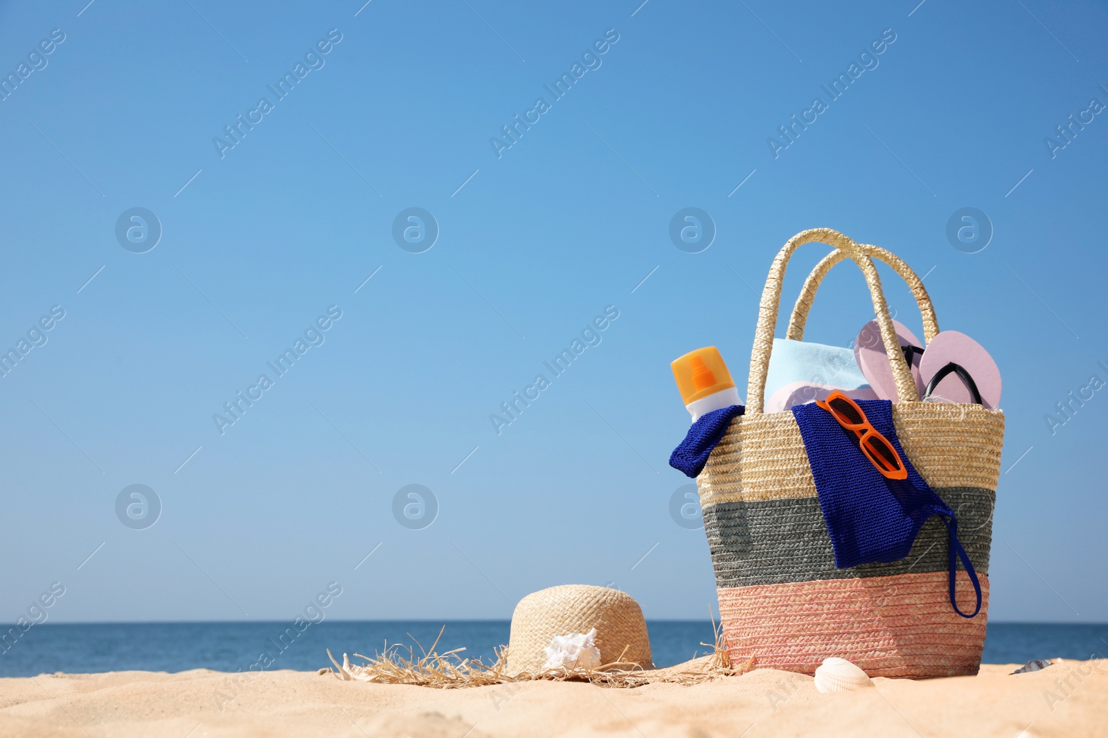 Photo of Bag with beach accessories and hat on sand near sea. Space for text