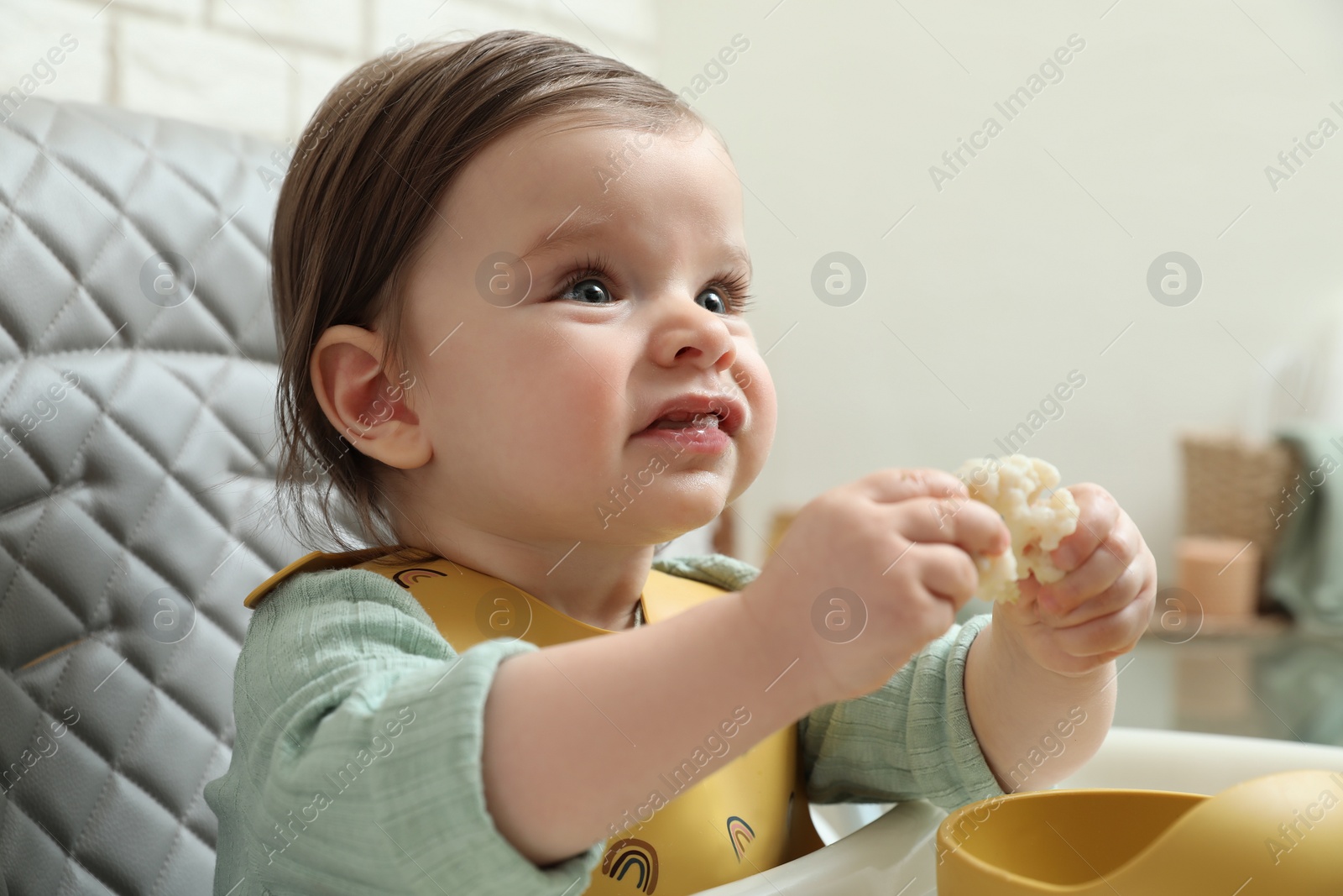 Photo of Cute little baby eating healthy food in high chair indoors