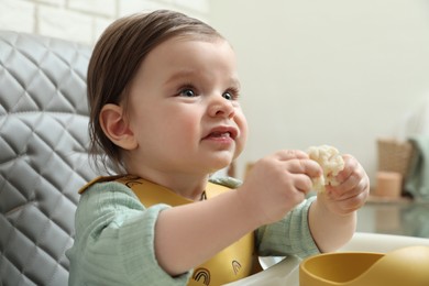 Photo of Cute little baby eating healthy food in high chair indoors