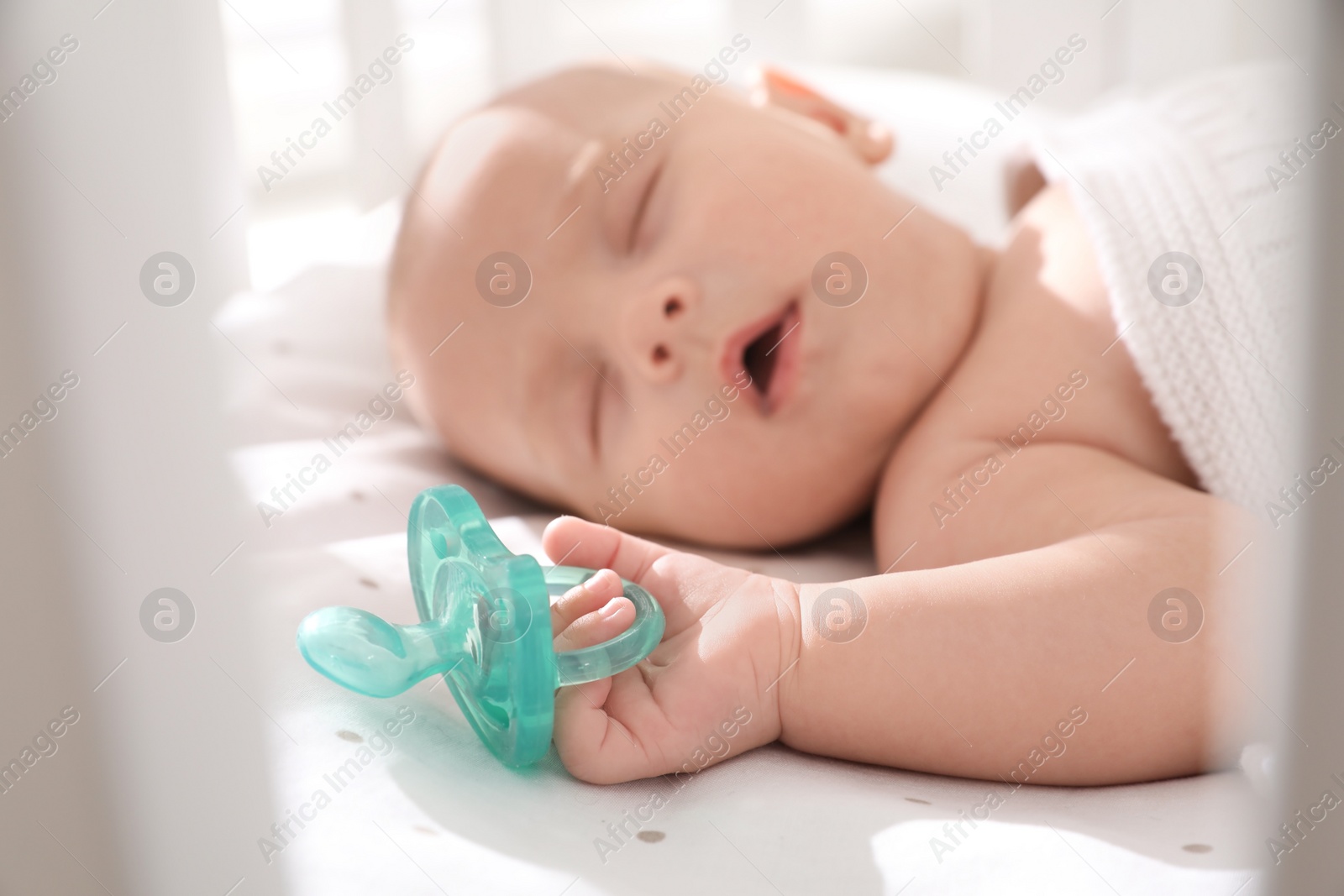 Photo of Cute little baby sleeping in crib, focus on hand with pacifier