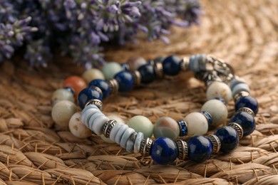 Photo of Beautiful bracelets with gemstones on wicker mat, closeup