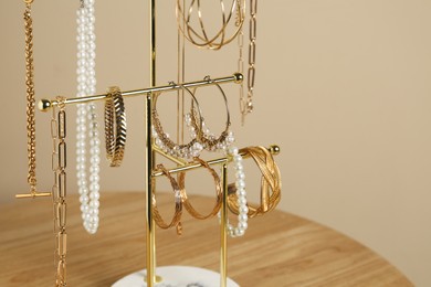 Photo of Holder with set of luxurious jewelry on wooden table near beige wall, closeup. Space for text