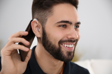Photo of Young man with hearing aid talking on phone indoors