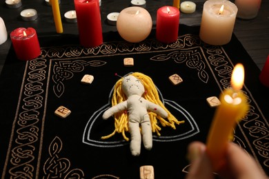 Voodoo doll pierced with pins and woman holding candle above black mat, closeup. Curse ceremony