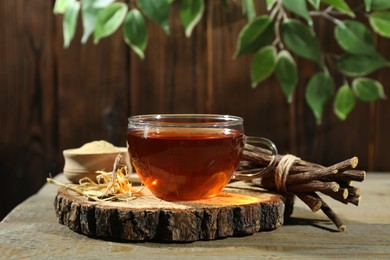 Photo of Aromatic licorice tea in cup, dried sticks of licorice root and powder on wooden table