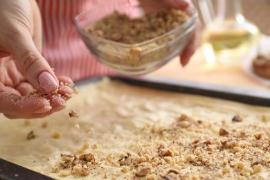 Making delicious baklava. Woman adding chopped nuts to dough, closeup