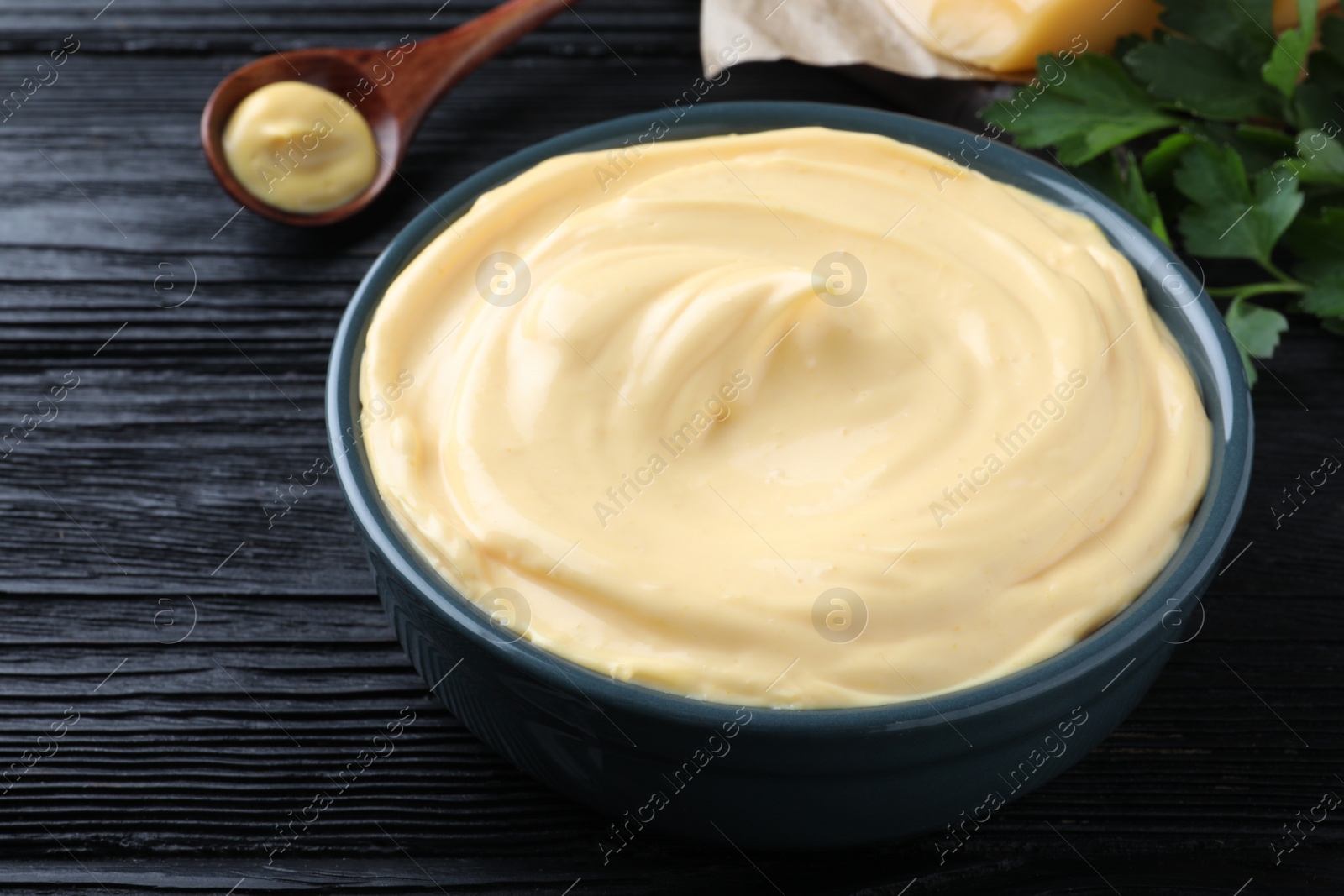 Photo of Tasty cheese sauce in bowl on black wooden table, closeup
