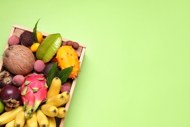 Photo of Different tropical fruits in wooden box on green background, top view. Space for text