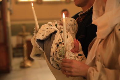 Stryi, Ukraine - September 11, 2022: Parents holding child and candles during baptism ceremony in Assumption of Blessed Virgin Mary cathedral, closeup
