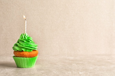 Photo of Delicious birthday cupcake with candle on light background