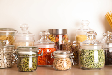 Glass jars with different types of groats on wooden shelf