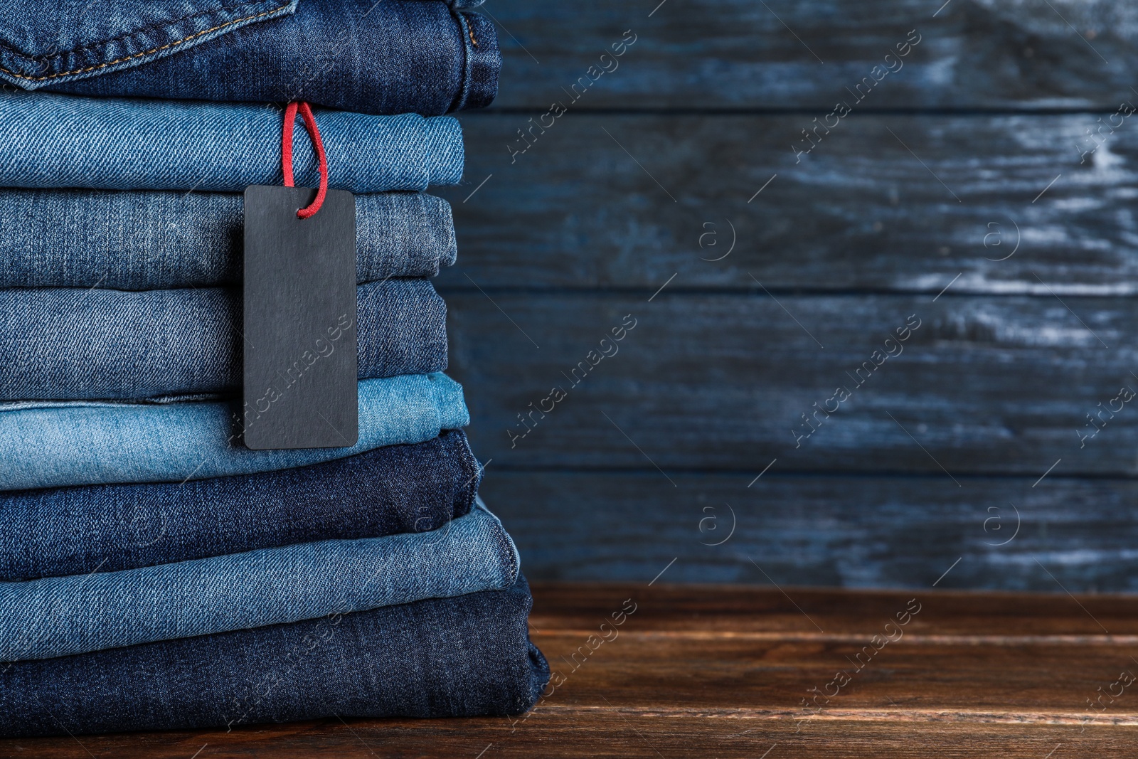 Photo of Stack of different jeans with tag on wooden table. Space for text