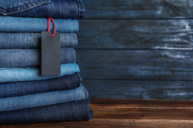 Stack of different jeans with tag on wooden table. Space for text