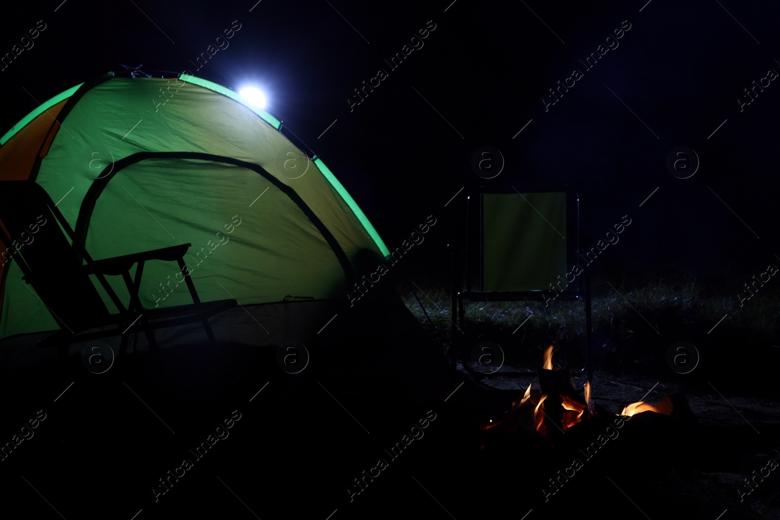 Photo of Bonfire and folding chairs near camping tent outdoors at night