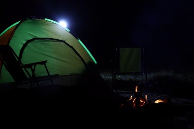 Bonfire and folding chairs near camping tent outdoors at night