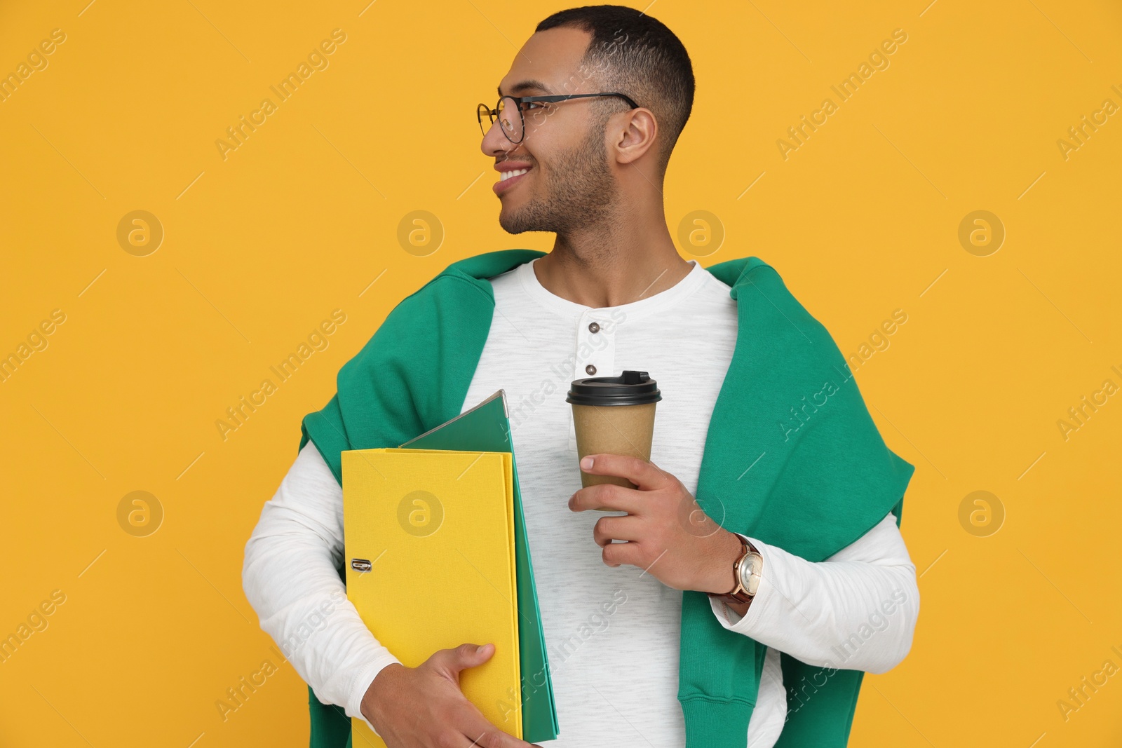 Photo of Happy young intern holding notebooks, cup of hot drink on orange background