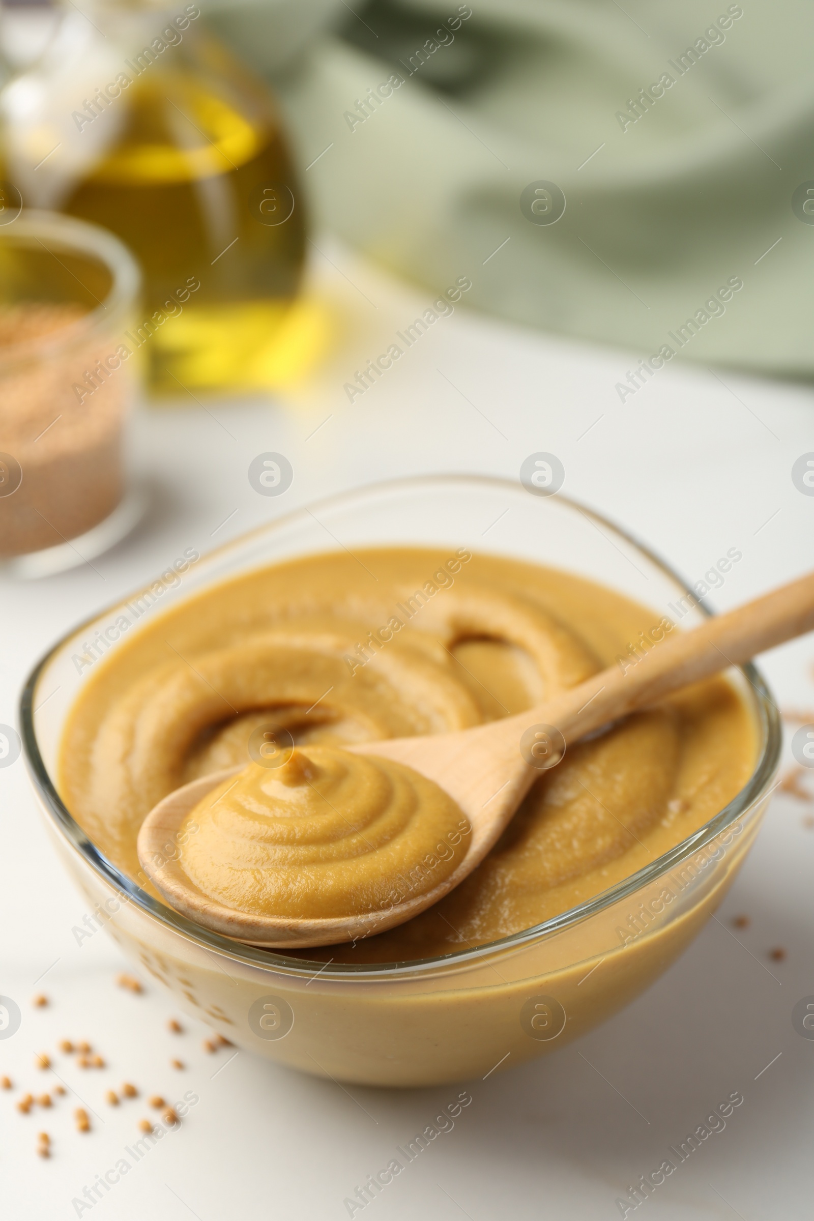 Photo of Spoon and glass bowl with tasty mustard sauce on white table