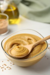 Spoon and glass bowl with tasty mustard sauce on white table