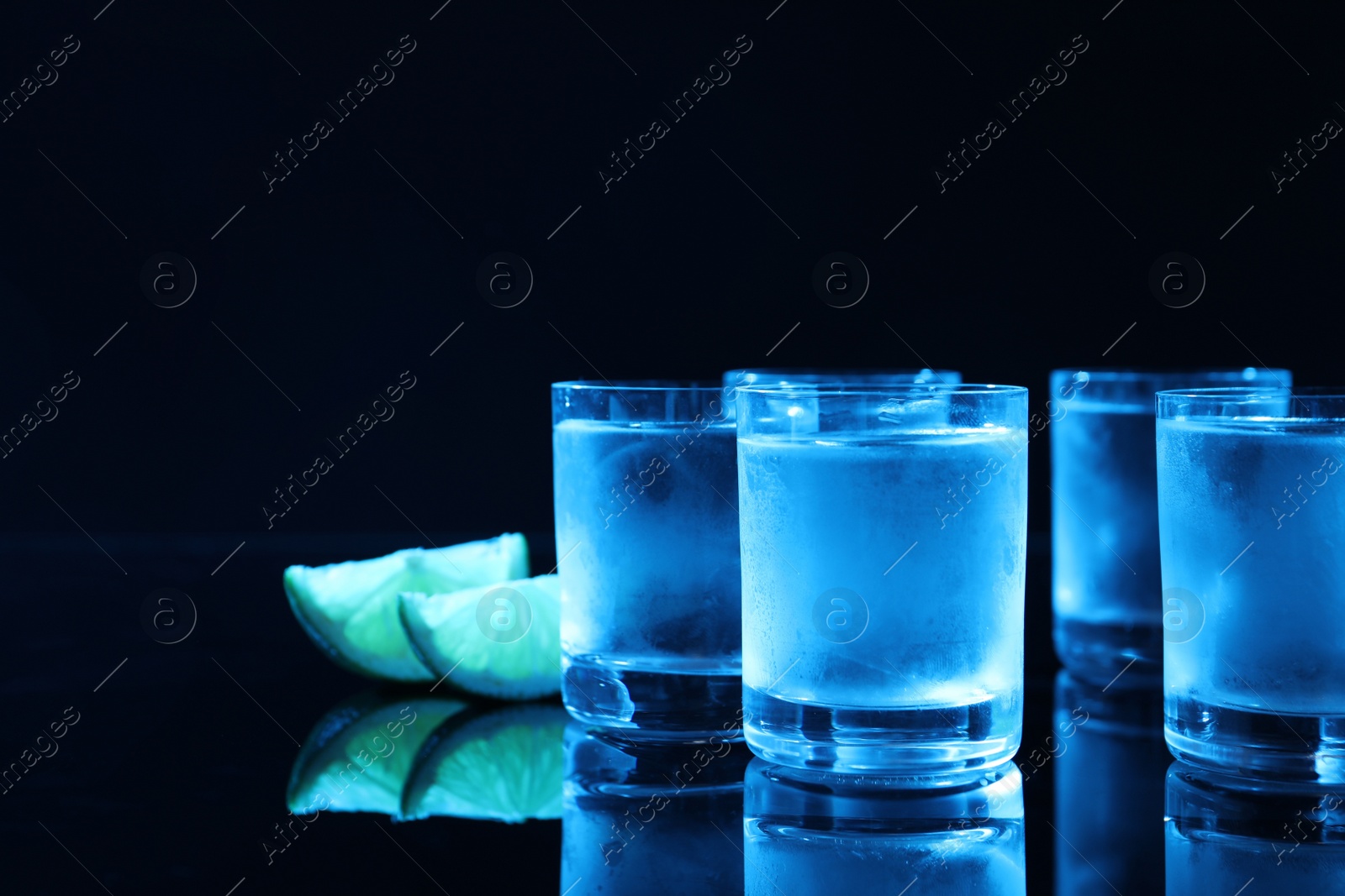 Photo of Shot glass of vodka with lime slices on dark background, space for text