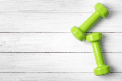Bright dumbbells and space for text on wooden background, flat lay. Home fitness