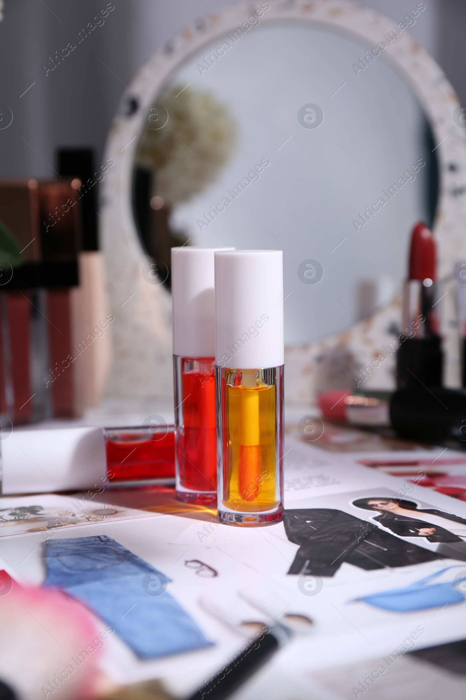 Photo of Bright lip glosses among different cosmetic products and fashion magazine on table indoors