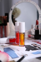 Bright lip glosses among different cosmetic products and fashion magazine on table indoors