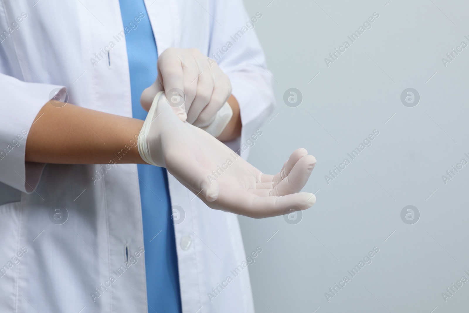 Photo of Doctor putting on medical gloves against light grey background, closeup