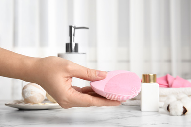 Woman holding face cleansing brush over marble table, closeup. Cosmetic accessory