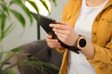Photo of Woman with tablet wearing smart watch at home, closeup